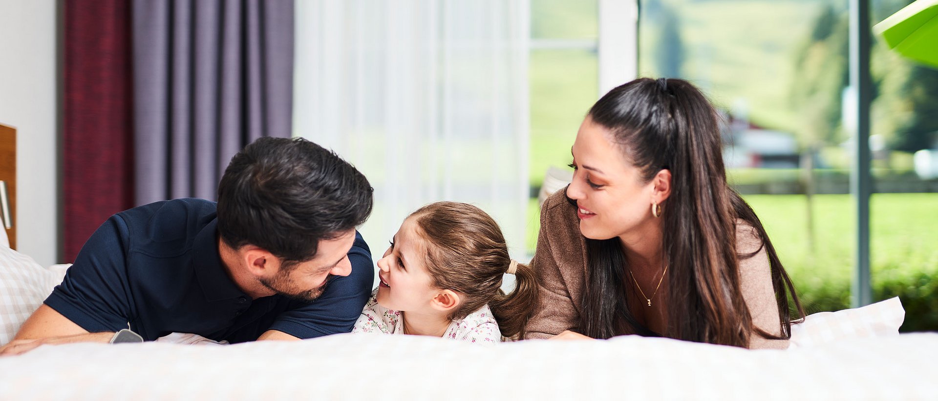 Familie liegt gemeinsam auf einem Bett in einem hellen Zimmer