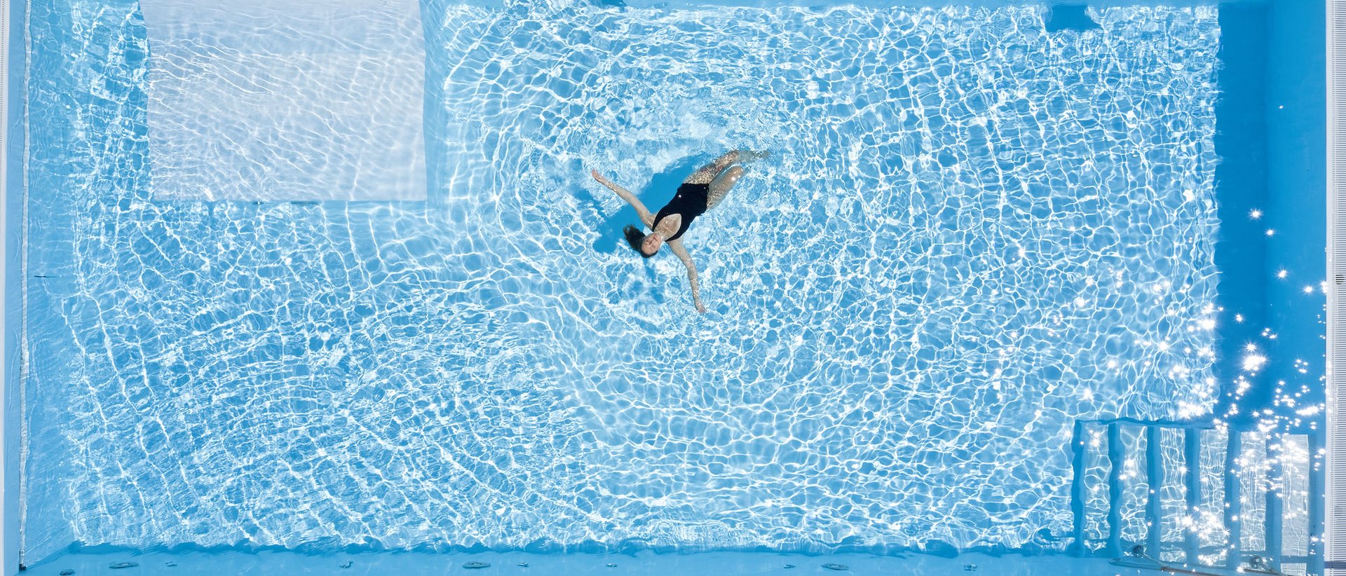 Alpin Lodges Oberjoch – Wellness & Aktivsein Frau schwimmt entspannt in klarem blauen Pool von oben gesehen