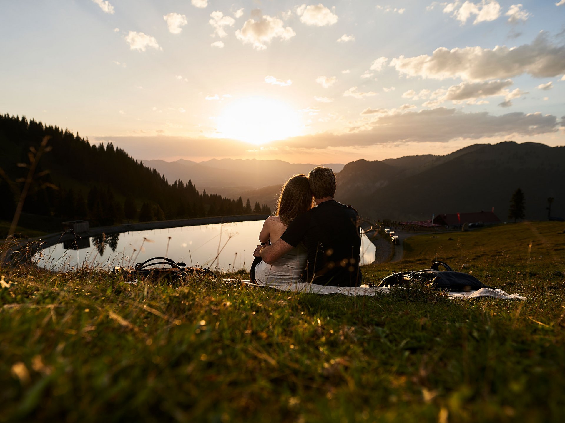 Appartement-Hotel im Allgäu: Erlebnisse Paar sitzt bei Sonnenuntergang an einem Bergsee